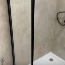 PGH - Kabina prysznicowa z czarnymi profilami i brodzikiem, wykończona płytkami imitującymi marmur.