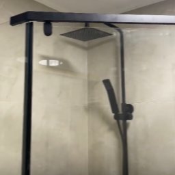 PGH - Nowoczesna kabina prysznicowa z czarnymi profilami i deszczownicą w wykończonej łazience z beżowymi płytkami.