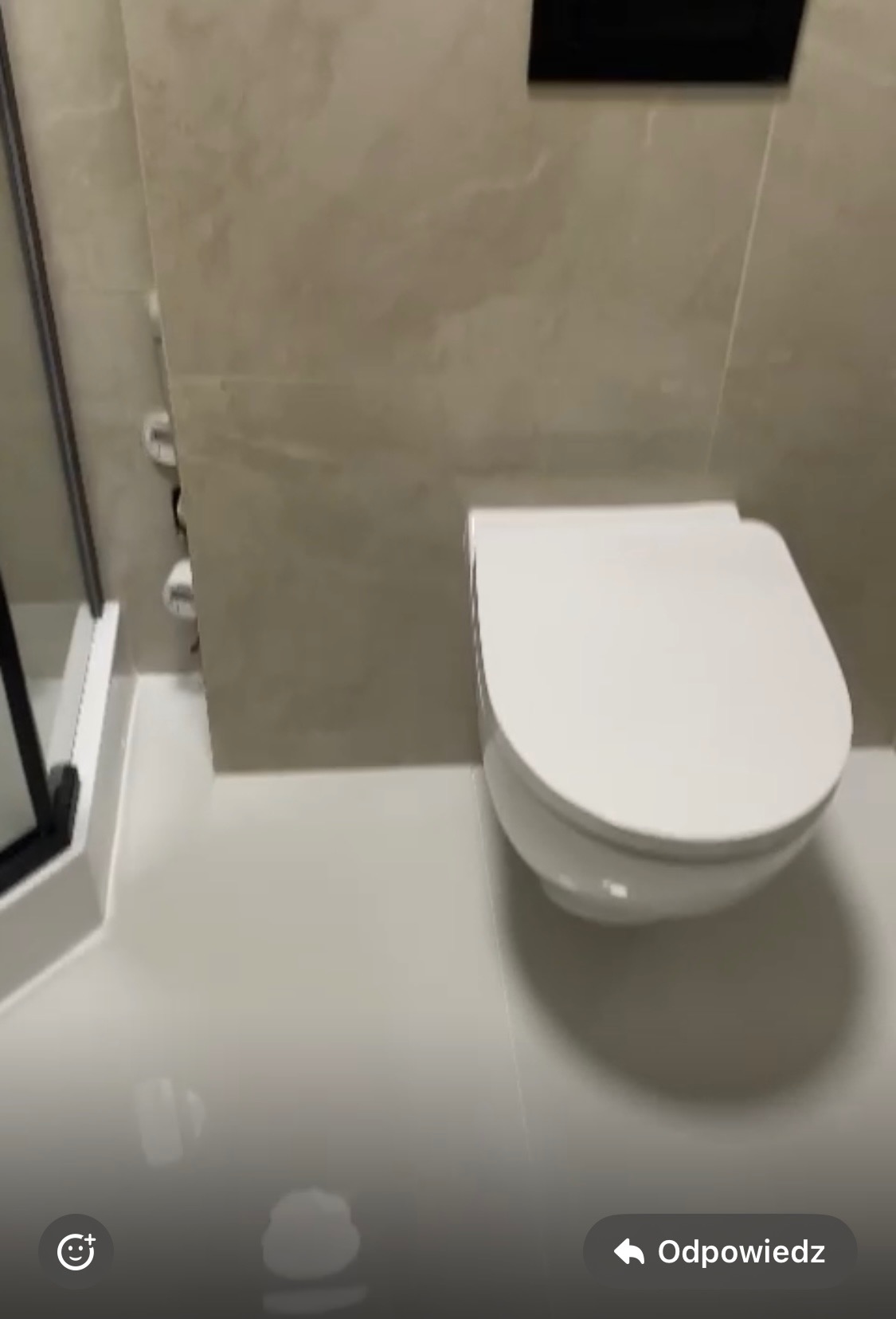 Nowoczesna, podwieszana toaleta w wykończonej łazience z beżowymi płytkami i czarnym panelem sterującym spłuczką.