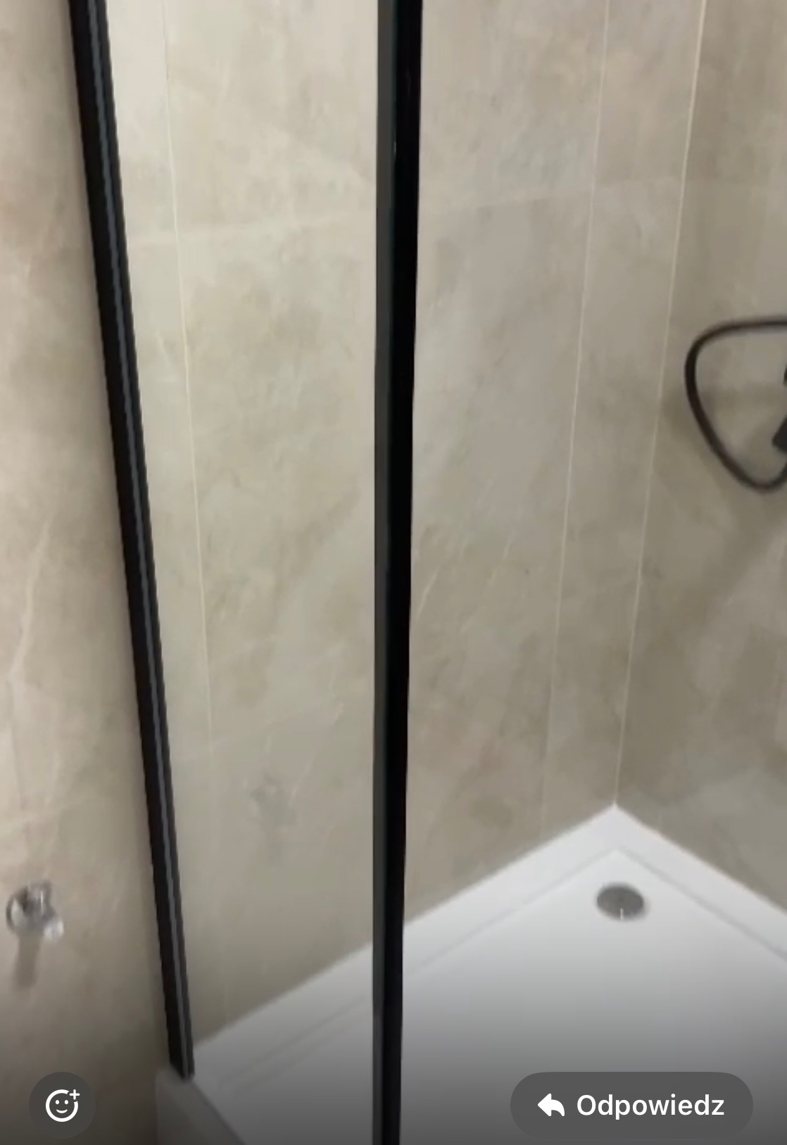 Kabina prysznicowa z czarnymi profilami i brodzikiem, wykończona płytkami imitującymi marmur.