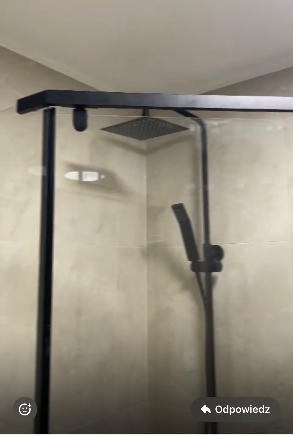 Nowoczesna kabina prysznicowa z czarnymi profilami i deszczownicą w wykończonej łazience z beżowymi płytkami.