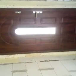 Brązowe drzwi wejściowe z szybą, osadzone w ościeżnicy wypełnionej pianką montażową, widoczne ślady prac wykończeniowych na ścianach i podłodze z płytek.