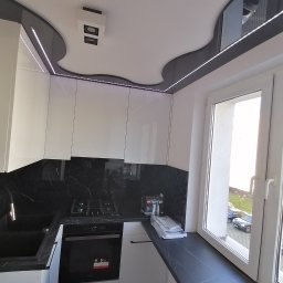 Rafal - Nowoczesna kuchnia z białymi szafkami, czarnym blatem i marmurowym backsplashiem, oświetleniem LED pod sufitem i oknem z widokiem na zewnątrz.