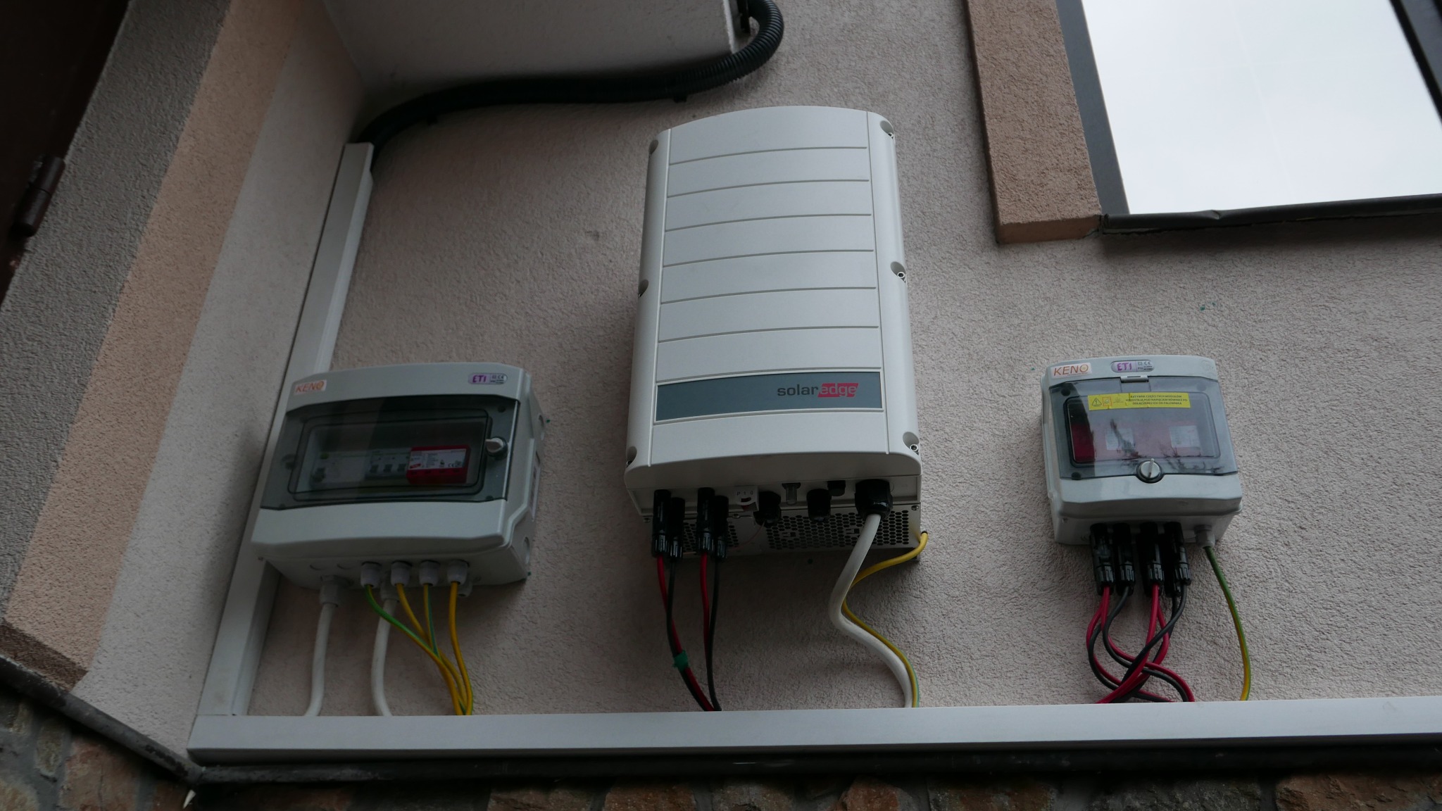 Instalacja elektryczna z inwerterem SolarEdge i skrzynkami zabezpieczeń na elewacji budynku.
