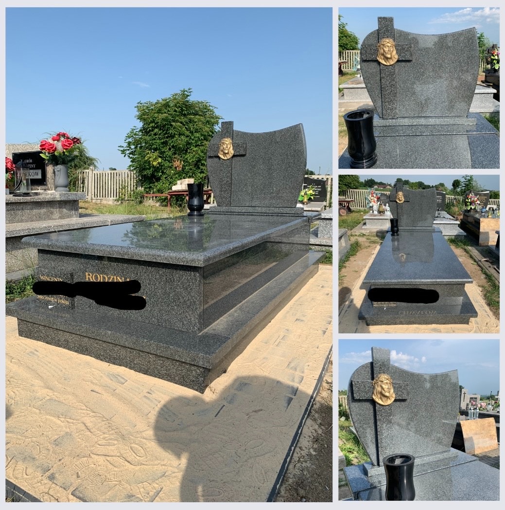 Granitowy nagrobek rodzinny z krzyżem i wizerunkiem Jezusa, umieszczony na cmentarzu, widoczny z perspektywy pieszego na piaskowej ścieżce.