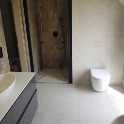 Sebastian Krawitowski Spec-Bud - Nowoczesna łazienka po remoncie: kabina prysznicowa typu walk-in z czarnymi profilami, podwieszana toaleta i umywalka nablatowa na szafce w odcieniach szarości.