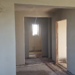 Świeżo otynkowane ściany wewnątrz budynku, widoczne instalacje grzewcze podłogowe, surowy stan wykończenia.