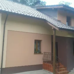 Elewacja domu po remoncie, z dwukolorowym malowaniem ścian i nową balustradą przy wejściu.