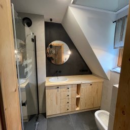 ELCOM - INSTALACJE ELEKTRYCZNE - Nowoczesna łazienka w skandynawskim stylu z drewnianą szafką pod umywalką, okrągłym lustrem i kabiną prysznicową z napisem 'Apartament przy lesie'.