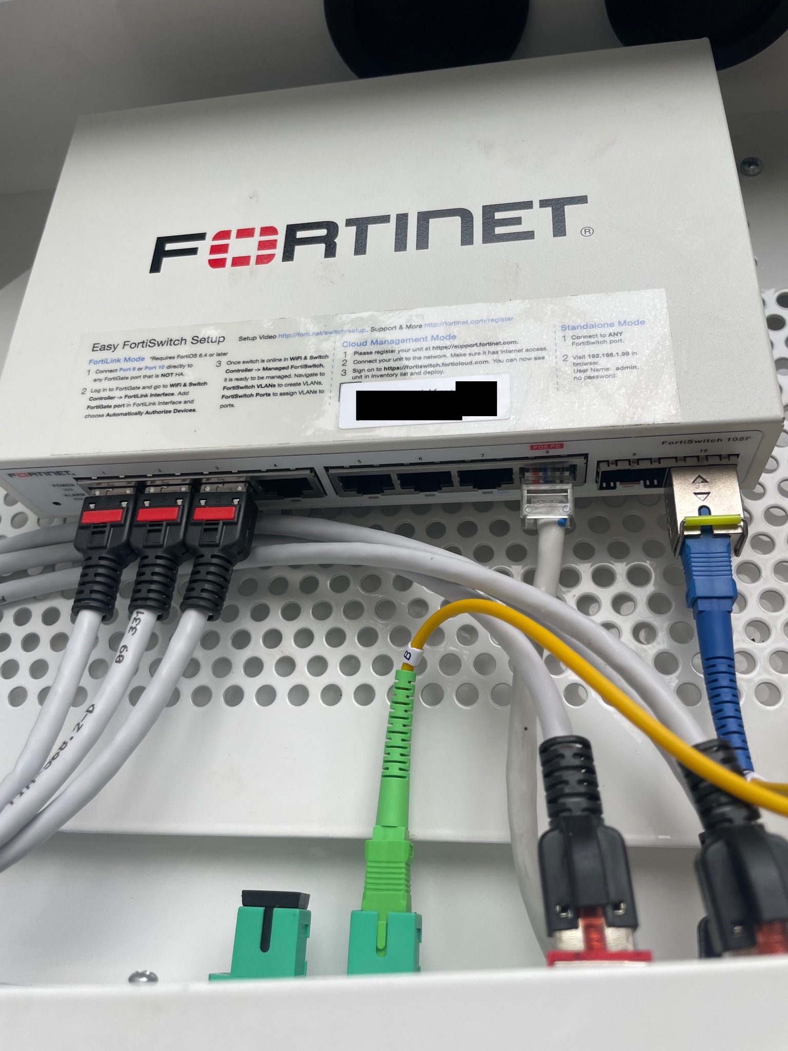 FortiSwitch 108F: Widok z bliska na panel połączeń z podłączonymi kablami Ethernet i światłowodowymi, etykietami i instrukcjami konfiguracji.