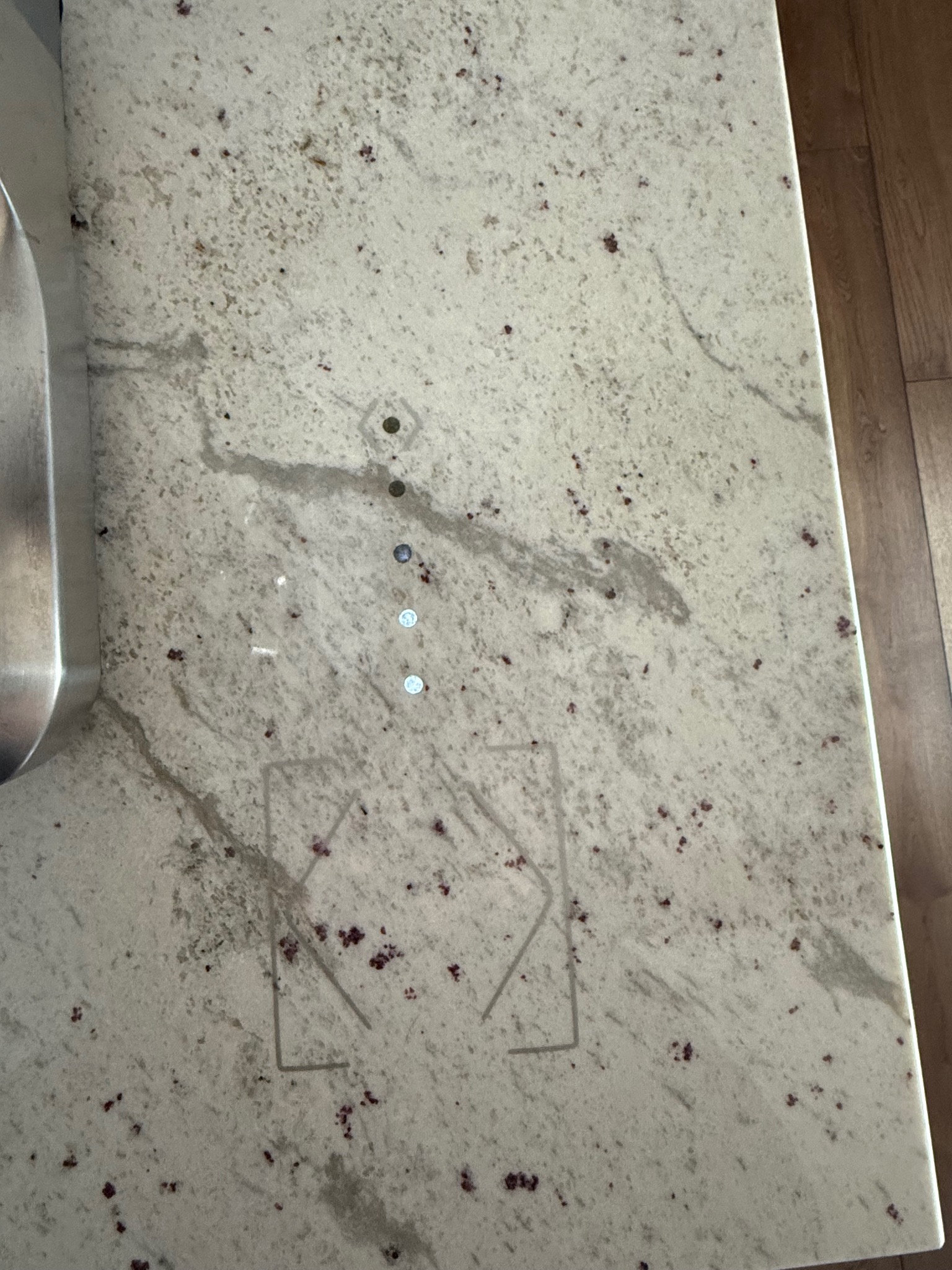 Biały, nakrapiany blat granitowy z widocznym zlewem oraz czterema otworami i zarysem kształtu rombu w dolnej części blatu.