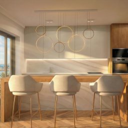Sun House Design Sp. z o.o. - Jasna kuchnia z wyspą i widokiem na morze. Trzy krzesła barowe przy drewnianej wyspie. Nad wyspą designerska lampa z okręgów. Parkiet w jodełkę. Nowoczesny design.