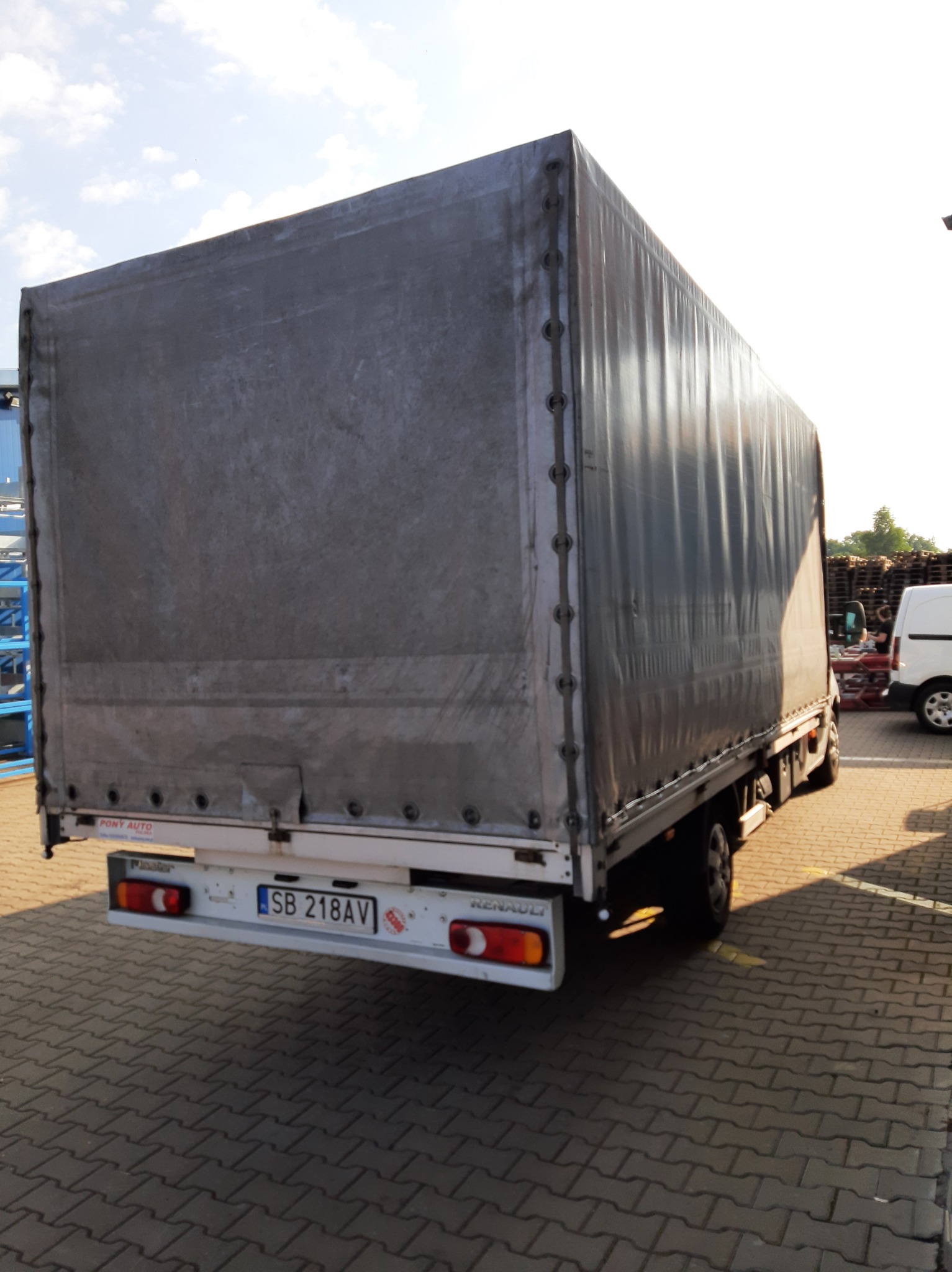 Tył samochodu dostawczego Renault z plandeką, widoczny numer rejestracyjny SB 218AV, zaparkowany na kostce brukowej w słoneczny dzień.