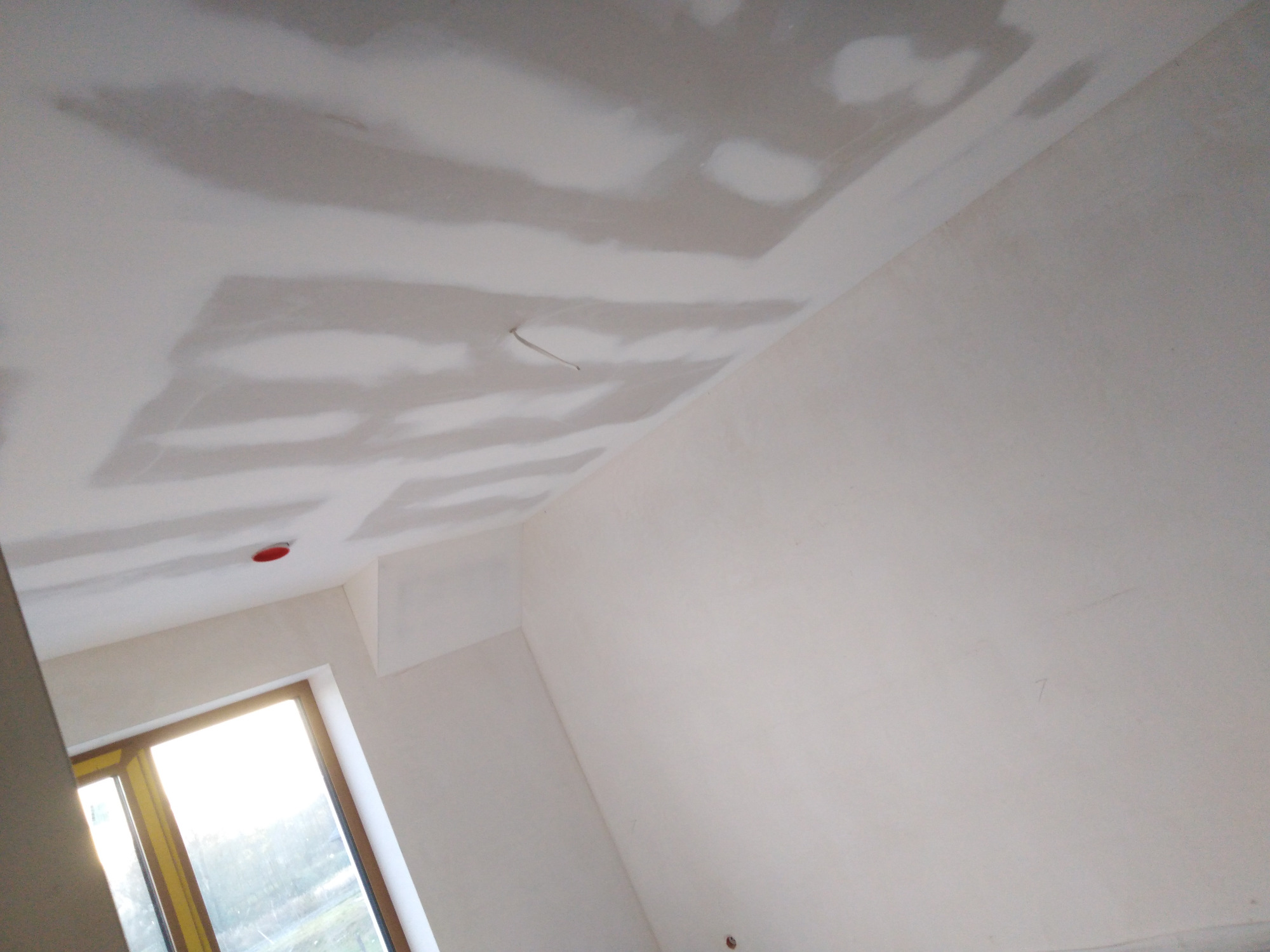 Nierównomiernie wyszpachlowany sufit z widocznymi smugami szpachli w nowym pomieszczeniu z oknem.