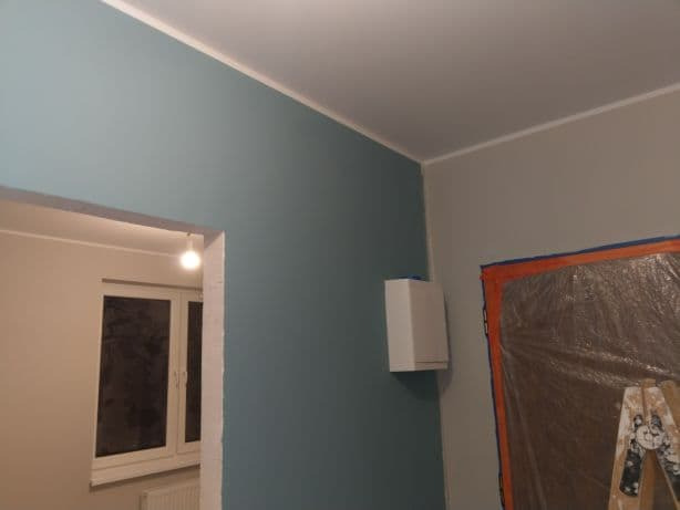 Fragment wnętrza po odświeżeniu koloru ścian, widoczna drabina malarska zabezpieczona folią okno oraz grzejnik.