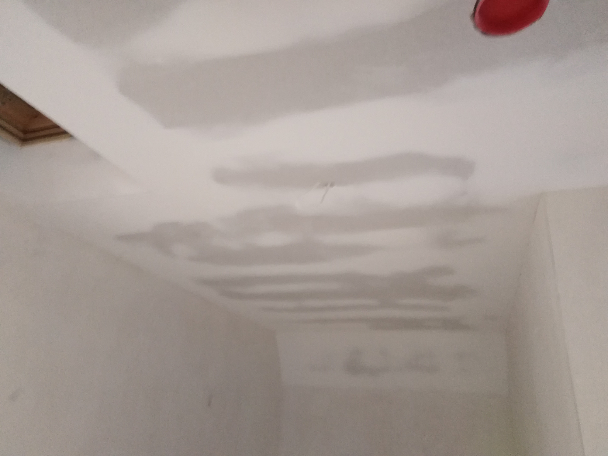 Nierównomiernie nałożona warstwa szpachli na suficie i ścianach, widoczne zacieki i niedoskonałości, czerwona puszka elektryczna wystająca z sufitu.