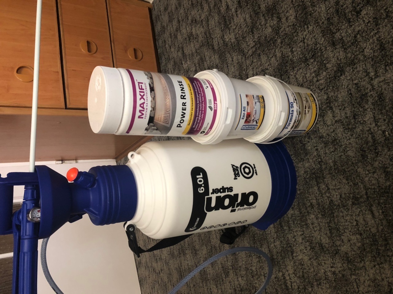 Środki czyszczące i opryskiwacz ciśnieniowy Orion Super 6.0L na dywanie, przygotowane do prania tapicerki.