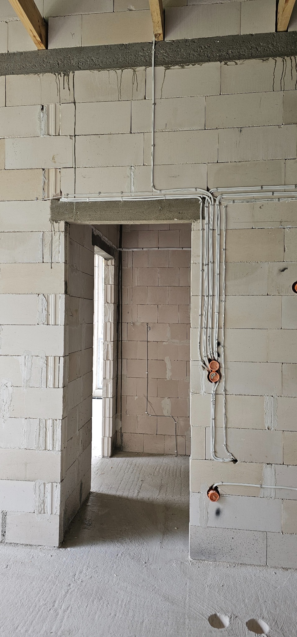 Wewnętrzna instalacja elektryczna w surowym budynku z betonu komórkowego, widoczne kable w peszlach prowadzone po ścianach i puszki instalacyjne w kolorze pomarańczowym.