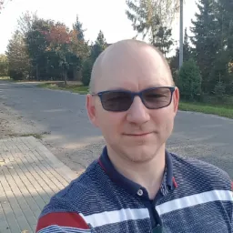 Mężczyzna w okularach przeciwsłonecznych, na zewnątrz, w tle ulica i drzewa. Autoportret.