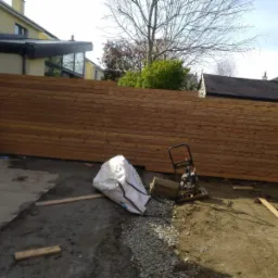 Montaż drewnianego ogrodzenia panelowego w Sieniawie, widoczna ubijarka wibracyjna i częściowo przygotowany teren.