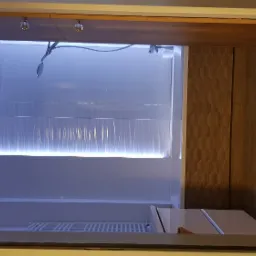 Nowoczesna kabina prysznicowa z podświetleniem LED, białe płytki z delikatnym wzorem i drewnopodobne panele na ścianie, chromowana bateria i deszczownica.