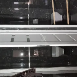 Nowoczesna łazienka z czarnymi płytkami imitującymi marmur, biała zabudowa wanny z frontami kasetonowymi i szklana kabina prysznicowa.