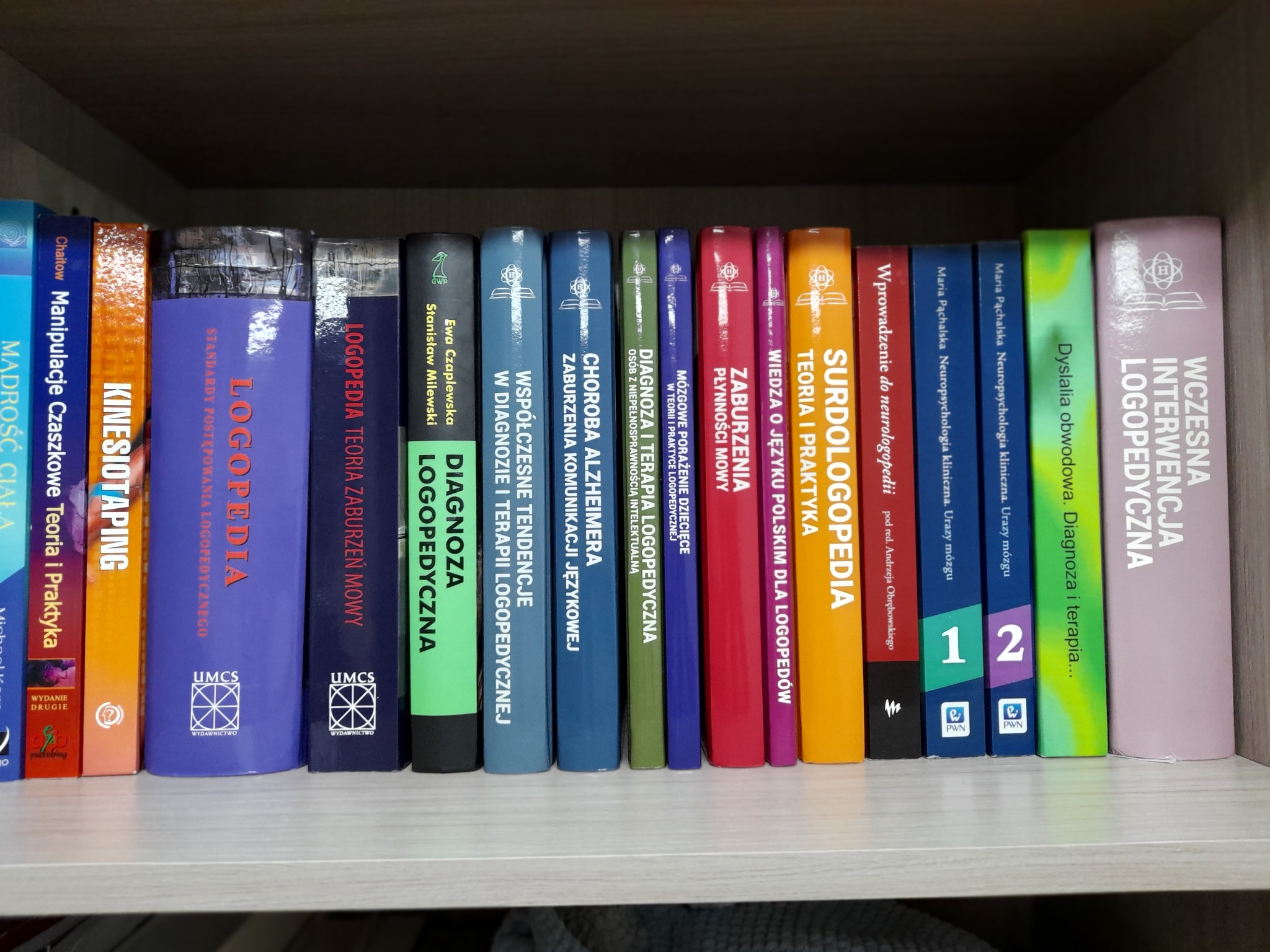 Półka z książkami o tematyce logopedycznej, widoczne tytuły dotyczące diagnozy, terapii i zaburzeń mowy, z logo wydawnictwa UMCS.