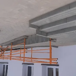 Ułożona szara kostka brukowa tworząca schody i chodnik, z widocznym rusztowaniem pomalowanym na pomarańczowo i aluminiową drabiną opartą o białą ścianę budynku.