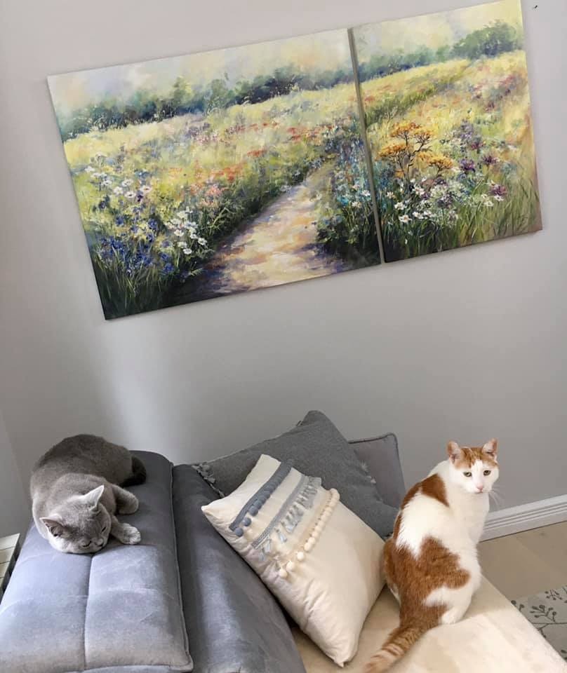 Diptych przedstawiający polną drogę wśród kwiatów, zawieszony nad szarą kanapą z dwoma kotami: śpiącym szarym i siedzącym rudym