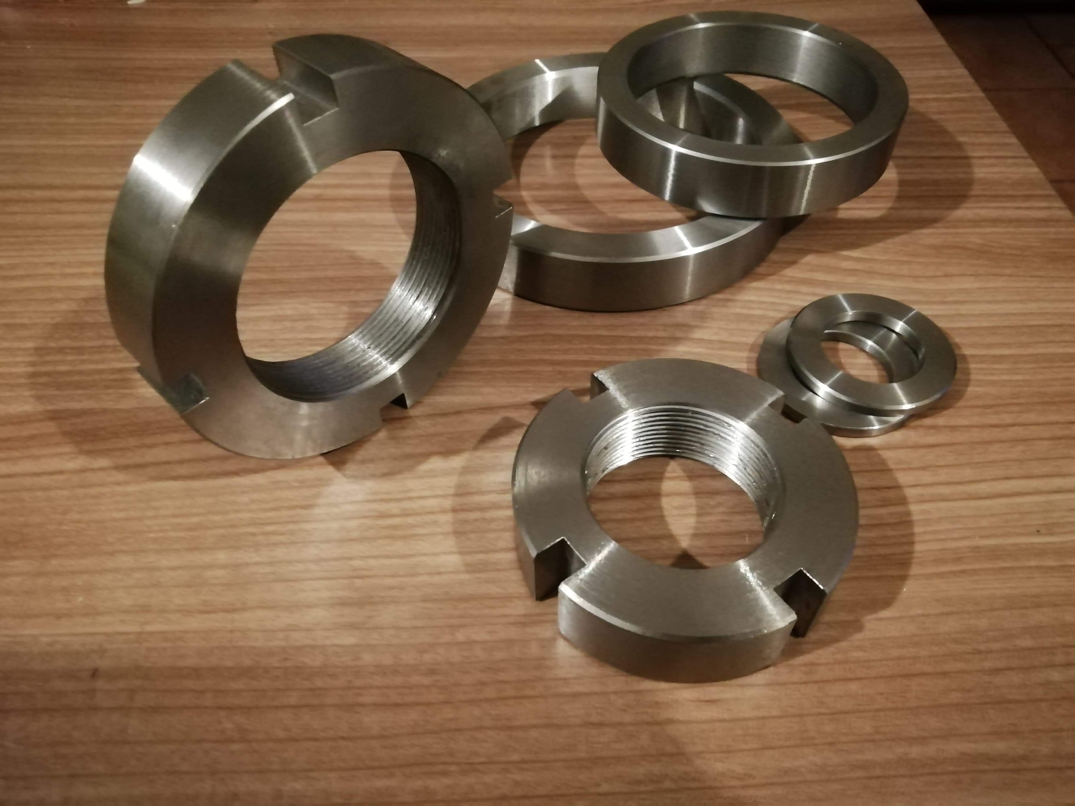 Srebrne, stalowe nakrętki z nacięciami, leżące na drewnianej powierzchni, widok z góry, różne rozmiary.