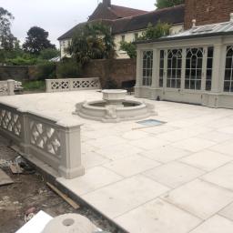 Cezary Pępczyński - Jasna, nowa patio z fontanną i ozdobnymi balustradami, przylegająca do oranżerii z przeszklonym dachem, widoczny brud na obrzeżach, ślady prac wykończeniowych.