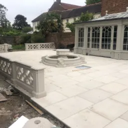 Jasna, nowa patio z fontanną i ozdobnymi balustradami, przylegająca do oranżerii z przeszklonym dachem, widoczny brud na obrzeżach, ślady prac wykończeniowych.