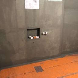 Cezary Pępczyński - Przygotowana do wykończenia łazienka z pomarańczową matą grzewczą na podłodze, wnęką w ścianie i wyprowadzonymi instalacjami hydraulicznymi, na ścianie widoczny plan techniczny.