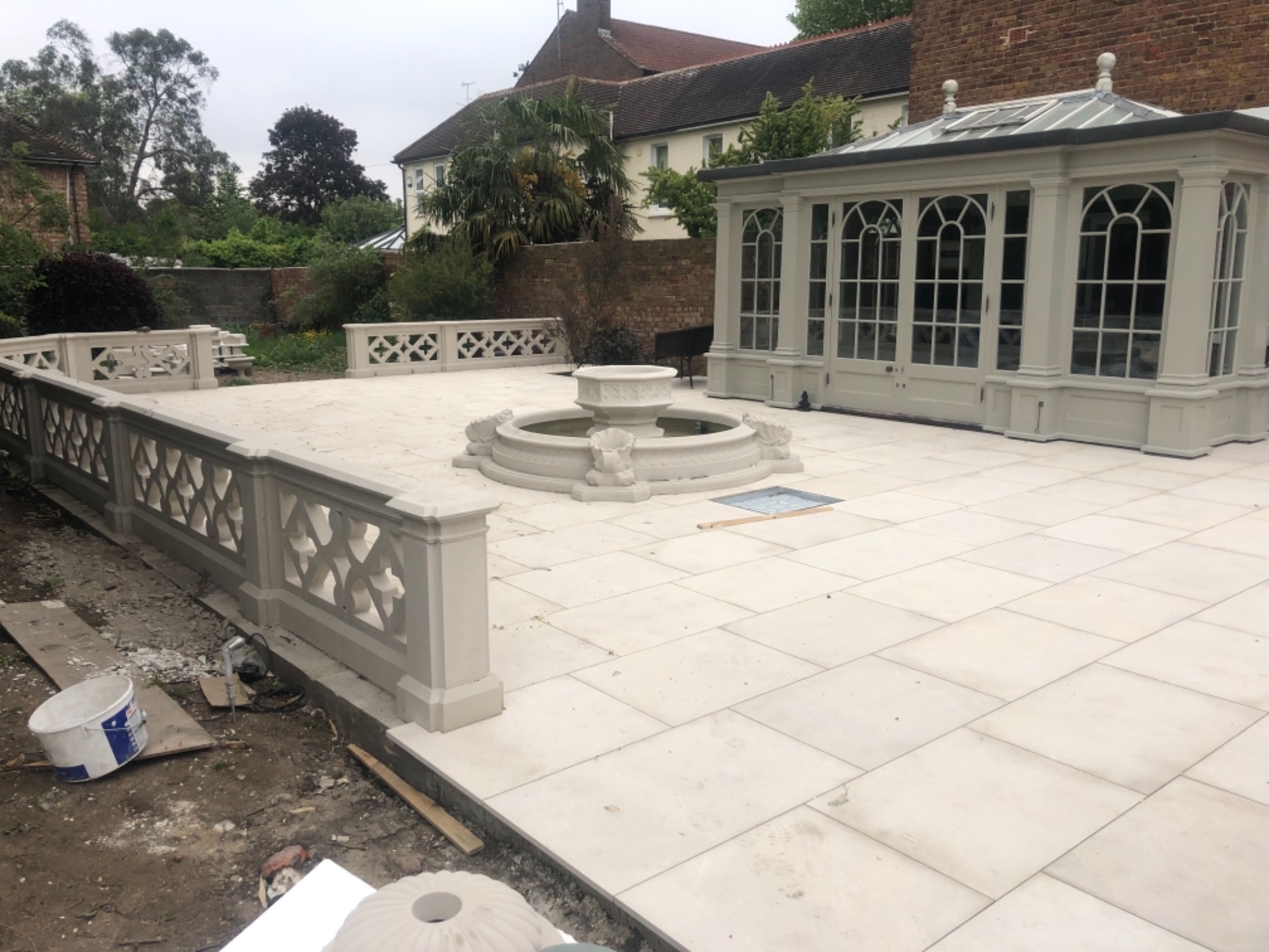 Jasna, nowa patio z fontanną i ozdobnymi balustradami, przylegająca do oranżerii z przeszklonym dachem, widoczny brud na obrzeżach, ślady prac wykończeniowych.