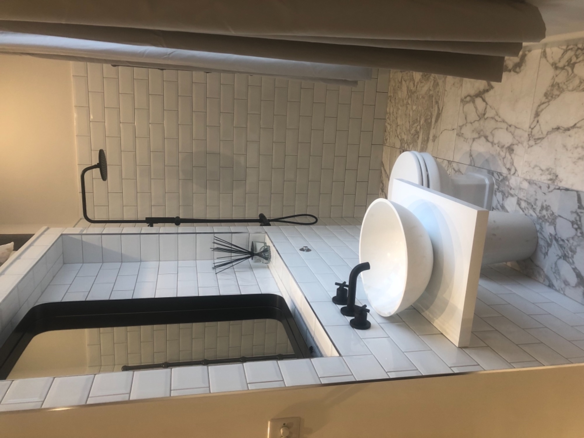 Nowoczesna łazienka z białą armaturą, czarną baterią umywalkową i marmurową ścianą, podkreślona przez białe, prostokątne płytki.