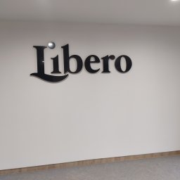 Usługi ogólno budowlane Sławomir gorzka. - Czarny napis 'Libero' zamontowany na białej ścianie w Olsztynie, widok z dołu, oświetlenie sufitowe.