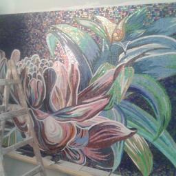 Usługi ogólno budowlane Sławomir gorzka. - Niedokończona mozaika ścienna przedstawiająca kwiaty, wykonana z drobnych, kolorowych płytek, z widoczną drabiną i fragmentem osoby w tle.