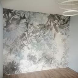 Usługi ogólno budowlane Sławomir gorzka. - Ściana z fototapetą w odcieniach szarości z motywem roślinnym, podświetlona nowoczesną lampą pierścieniową, widok na fragment parkietu i drzwi.