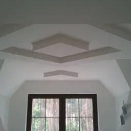 Białe poddasze z oknem i dekoracyjnymi, geometrycznymi elementami sufitowymi w kształcie rombów, pomalowane na biało.