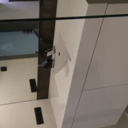 Biała szafka łazienkowa z umywalką i baterią, odbicie w lustrze z oświetleniem i gniazdkami elektrycznymi, widok z góry.