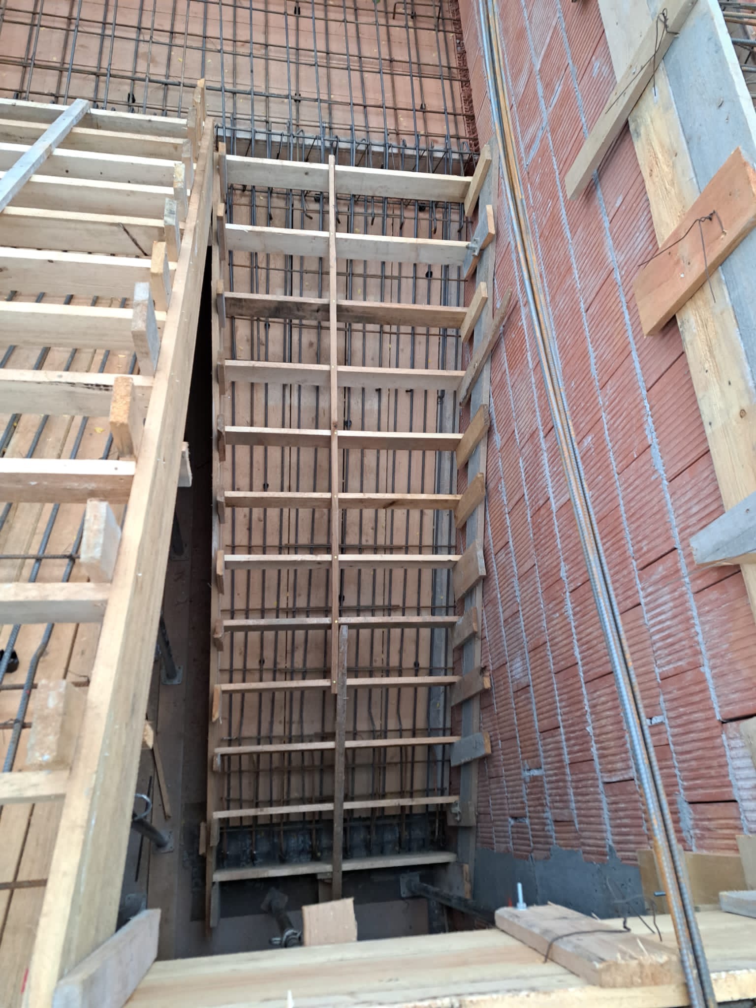 Szczegółowy widok szalunku schodów z drewnianych desek i stalowego zbrojenia, przygotowanego do zalania betonem, z widoczną konstrukcją schodów tymczasowych.