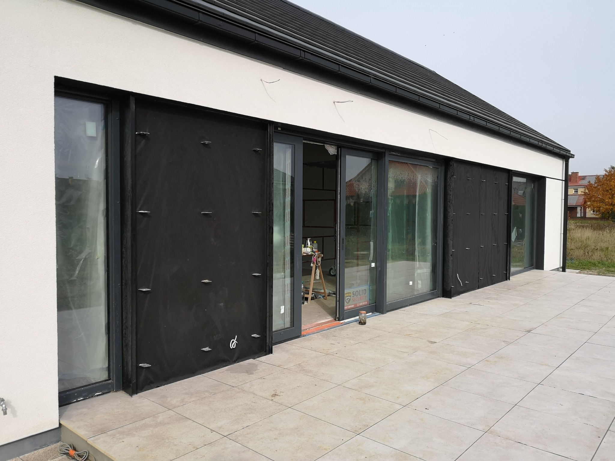 Montaż okien przesuwnych w nowoczesnym domu jednorodzinnym, widoczne zabezpieczenia folią i narzędzia pracy na tarasie.