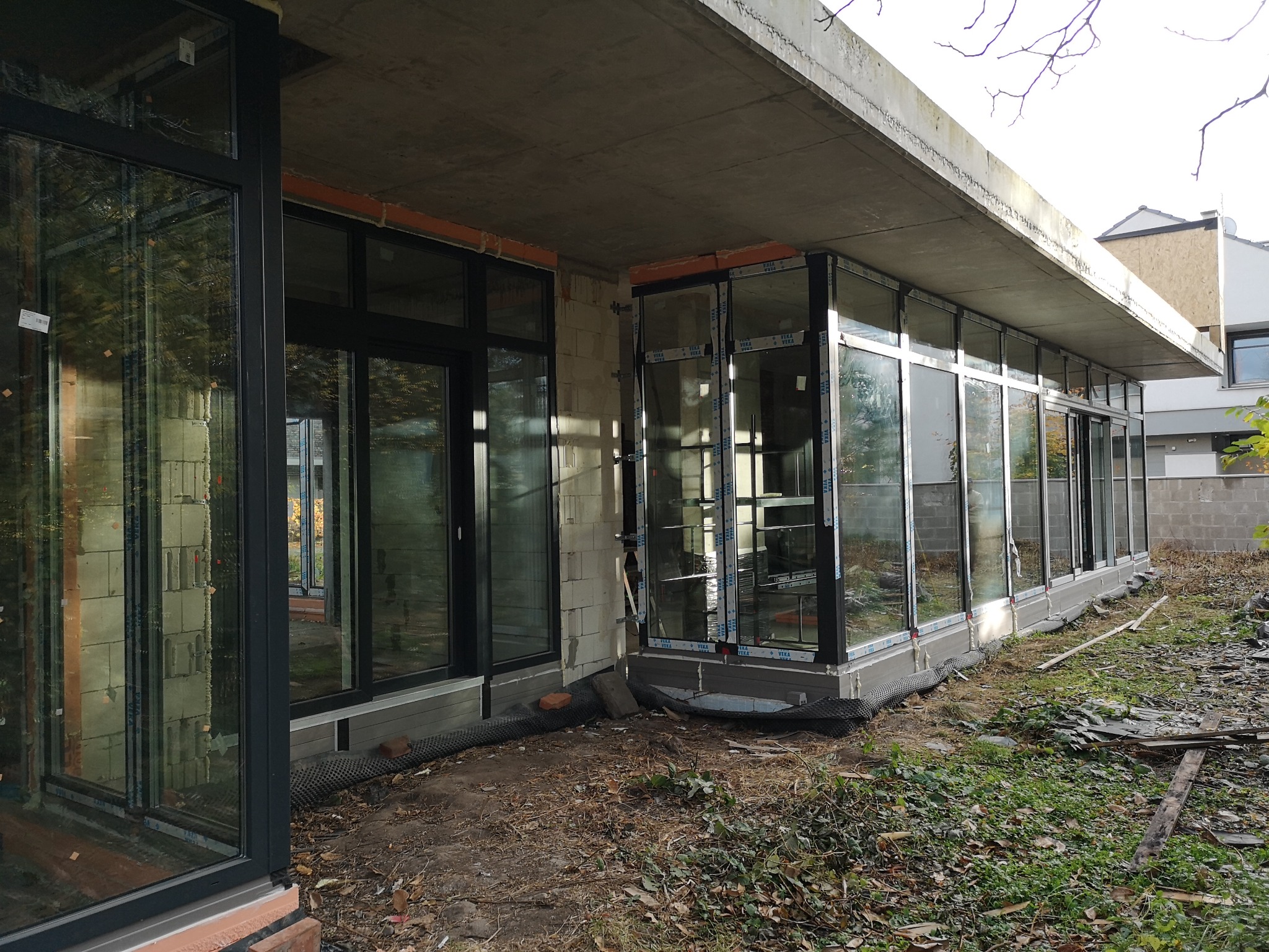 Montaż stolarki okiennej z czarnymi ramami w surowym stanie budynku, widoczne bloczki betonowe i niezabezpieczone podłoże.