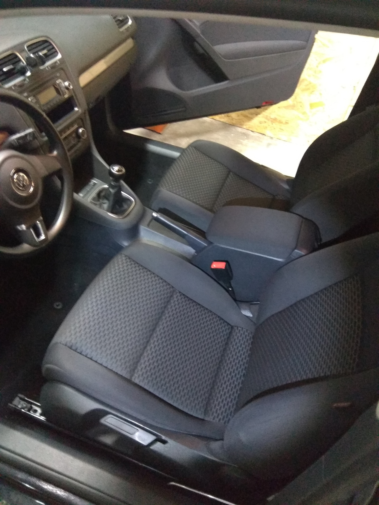 Wnętrze samochodu z widocznymi fotelami o ciemnej, teksturowanej tapicerce, dźwignią zmiany biegów i kierownicą z logo producenta. Ujęcie z wnętrza pojazdu, z otwartymi drzwiami i widocznym...