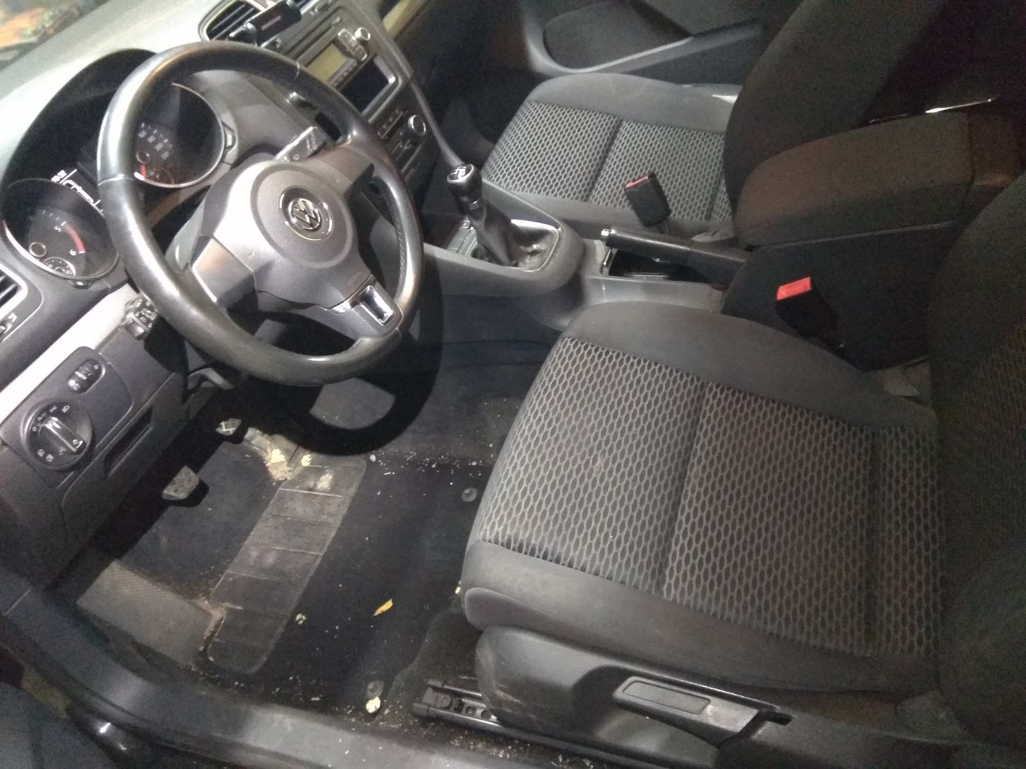 Wnętrze samochodu z widocznymi zabrudzeniami na podłodze i siedzeniach, wymagające czyszczenia; widoczna kierownica z logo Volkswagen.