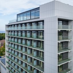Rafał Leoniewski Solutions - Wielopiętrowy budynek z balkonami z przezroczystymi balustradami, widok z góry na tle morza i lasu.
