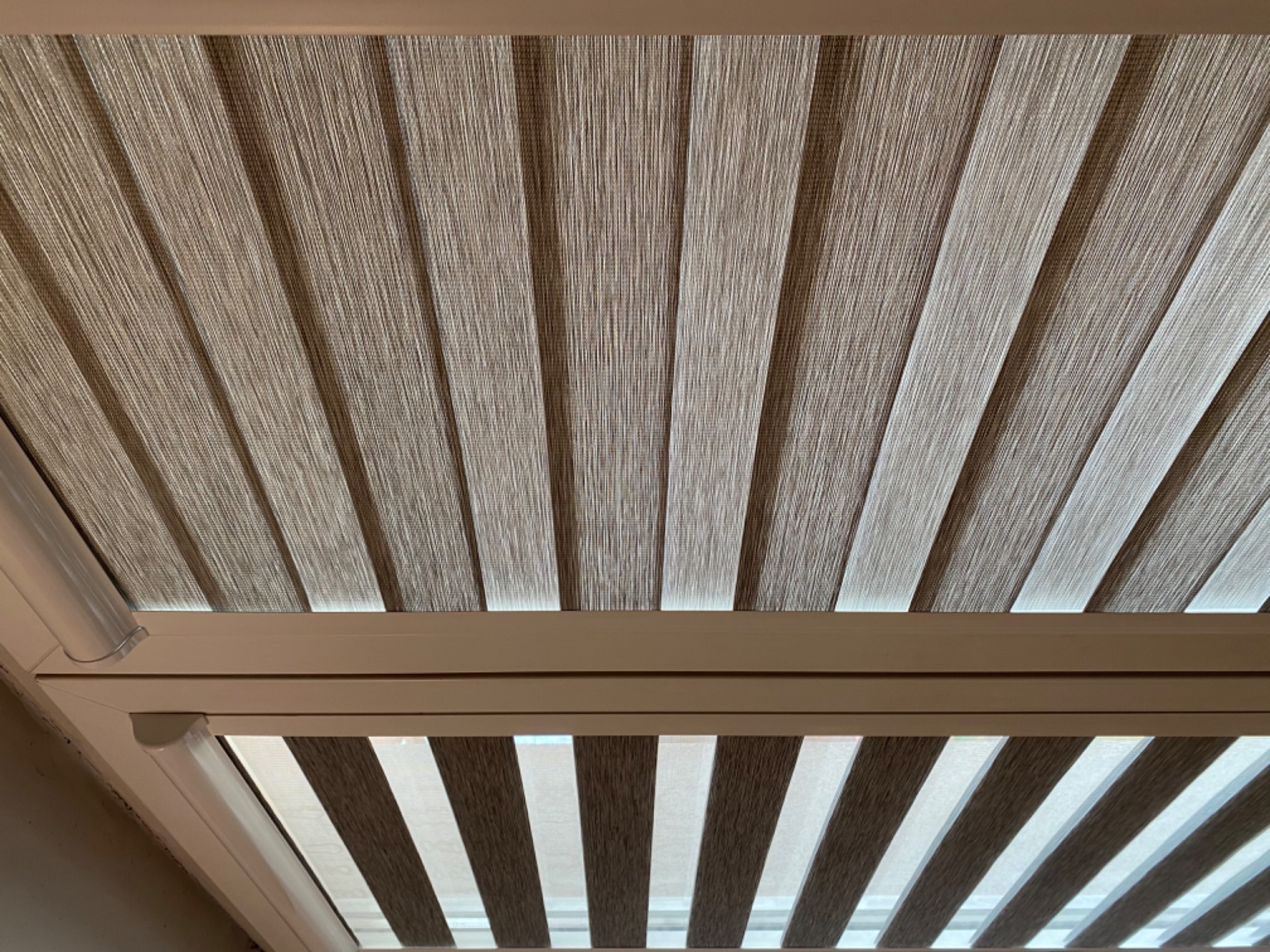 Beżowo-białe, pionowe listwy zaciemniające okno, widok od dołu w kierunku sufitu.