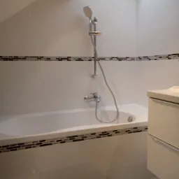 Biała, minimalistyczna łazienka z wanną obudowaną mozaiką, chromowaną baterią i słuchawką prysznicową, oświetlona punktowym światłem i doświetlona światłem dziennym z okna dachowego.