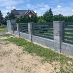 Nowoczesne ogrodzenie z szarych bloczków betonowych i poziomych, grafitowych przęseł metalowych, na tle domu z panelami słonecznymi i zieleni.