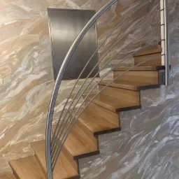 Spiralne schody z drewnianymi stopniami i metalową poręczą na tle ściany z efektem marmuru.